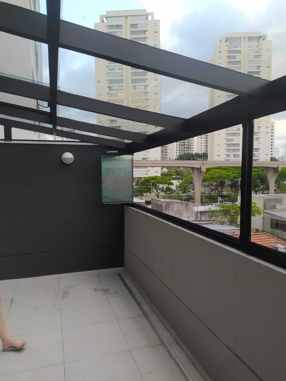 Cobertura de vidro com estrutura metálica preta em terraço residencial com vista urbana